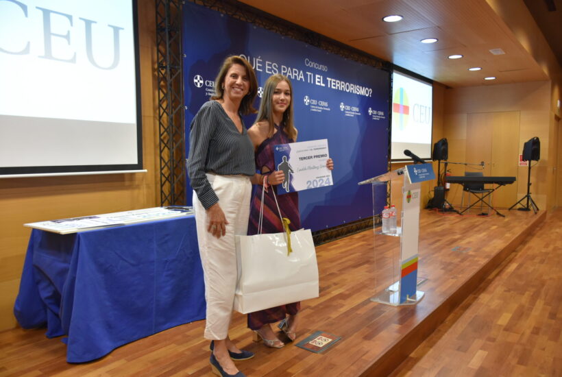 Two women standing on a stage holding bags and a sign