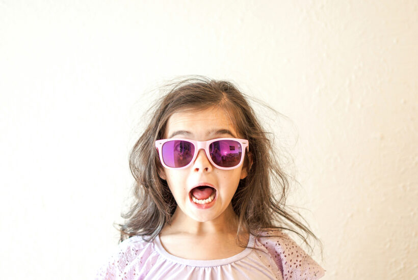 A girl wearing pink sunglasses and a white shirt with her mouth open