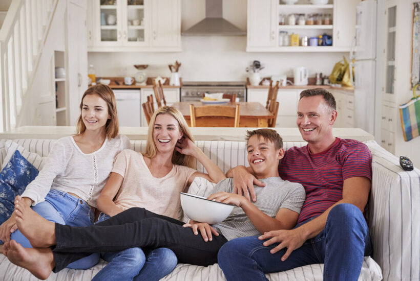 family with teenage children sitting on sofa watch PYRE24G 945x630 1 &bull; Cómo mejorar la convivencia con hijos adolescentes durante el verano